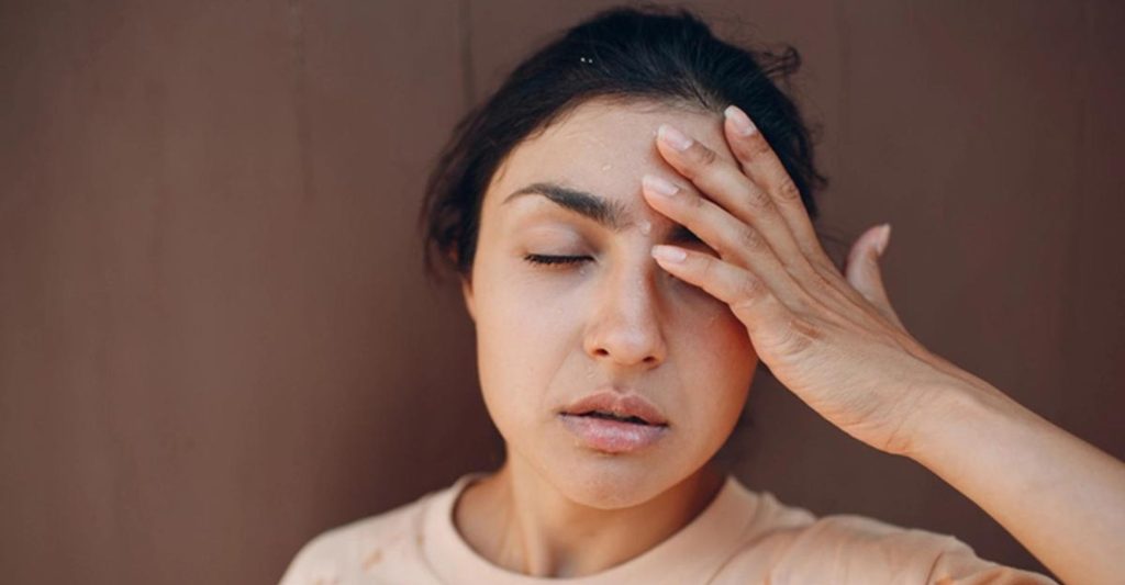 A woman holding her hand up to her head with sweat running along her brow.