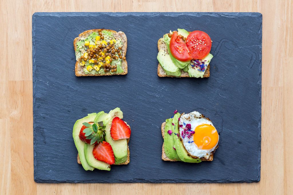 Four slices of avocado toast with different toppings: chickpeas, tomatoes, strawberries, and egg.