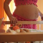 Pregnant woman standing in front of a bassinet with stuffed animals in it