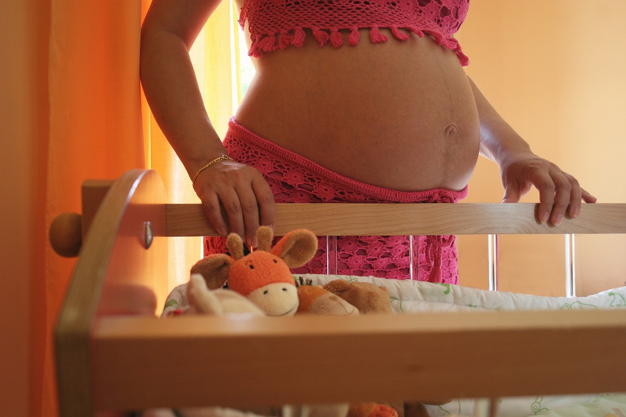 Pregnant woman standing in front of a bassinet with stuffed animals in it